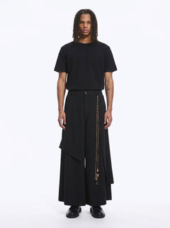 Man in black wrap-front hakama pants with a layered front panel and braided cord, black tee, full length, front view