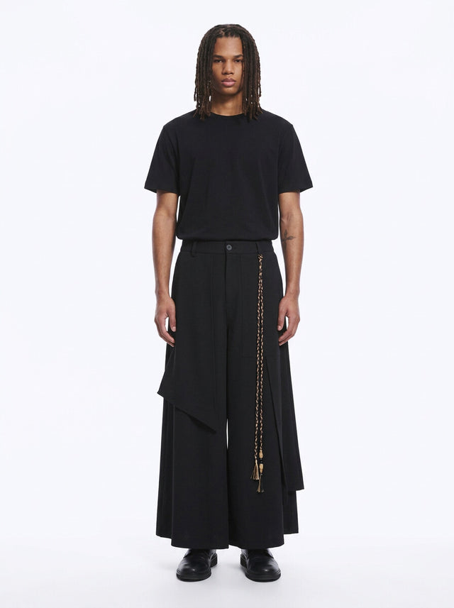 Man in black wrap-front hakama pants with a layered front panel and braided cord, black tee, full length, front view