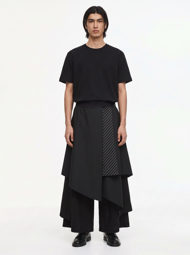 Double layered hakama pants in black on a model, front view: asymmetric skirt overlay with a pinstripe front panel over wide trousers