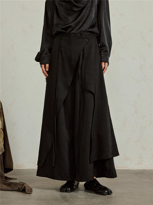 Dark cotton hakama pants, front: a wrap panel buttons at the waist and falls open over the wide leg, with long ties hanging down