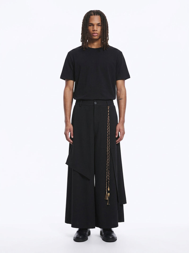 Man in black wrap-front hakama pants with a layered front panel and braided cord, black tee, full length, front view